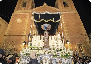Trono procesional iluminado con velas frente a la Iglesia de Nuestra Se&ntilde;ora de la Encarnaci&oacute;n durante la Semana Santa de Cuevas del Almanzora